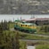 A vintage train turns at a bend next to a mountainside lake